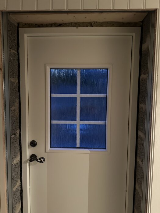 Ytterdörr installerad mellan murade väggar i en källare utan synlig tätningstejp eller isolering runt dörrkarmen.