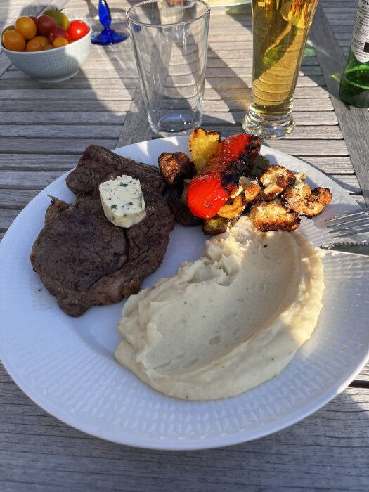Grillad entrecote med kryddsmör, potatispuré, rostad blomkål, grillade champinjoner och paprika på en tallrik utomhus.