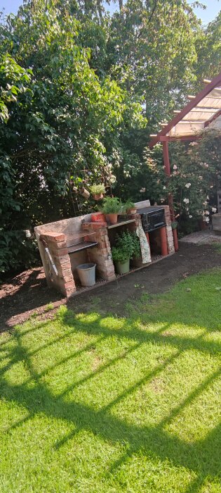 Hemmagjort utekök byggt av återvunna material, dekorerat med krukväxter under ett träd i trädgården.