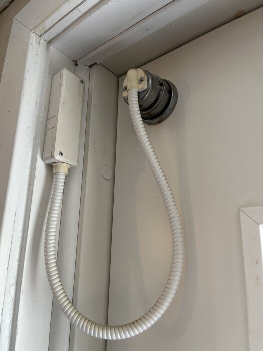 Ett dörrlarm med en vit spiralsladd fäst på en dörrkarm och kopplad till en sensor på dörren.