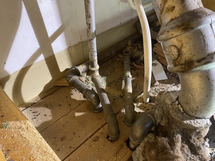 Rör och ledningar under diskho och element i ett hus. Gamla, rostiga rör på ett dammigt trägolv.