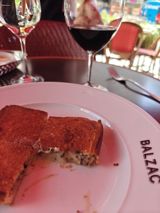 En tryffel croque monsieur serverad på en tallrik med ett glas rödvin i bakgrunden på ett cafébord.