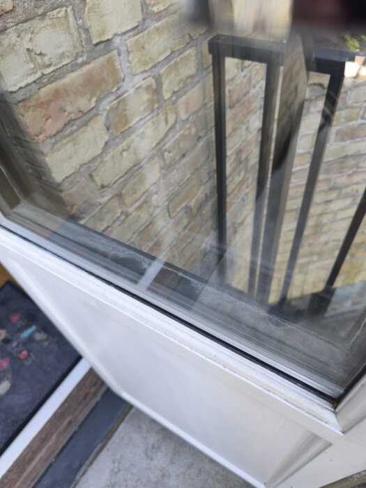 Närbild av en del av en vit pardörr med glas, synlig tegelvägg utanför och metallräcke.