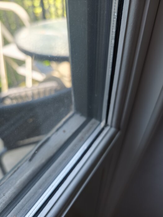 Närbild på glas och karm i den vänstra delen av en pardörr, med en suddig bakgrund som visar utemöbler.