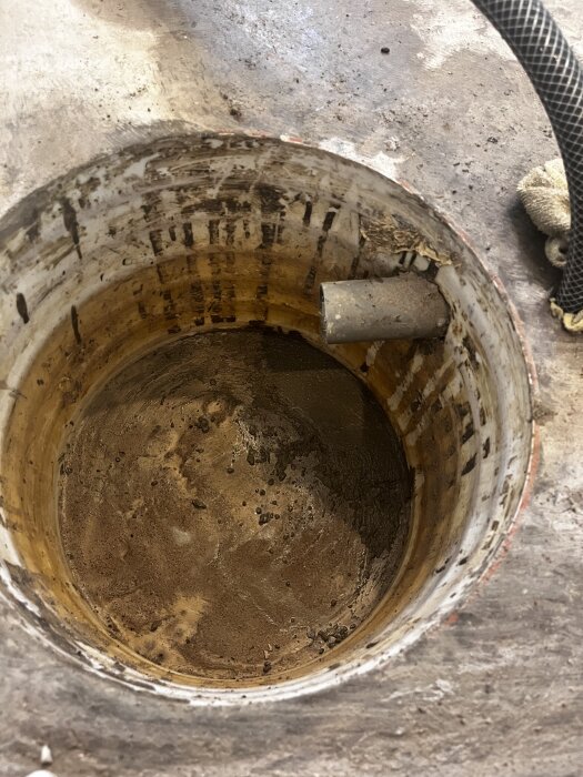 Pumpbrunn under renovering med smutsig insida, rör och slang ansluten på sidan, planerad för tätning och betonggjutning.