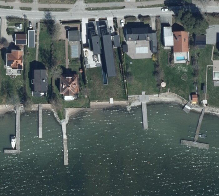 Flygbild över hus längs vattnet utan helikopterbrygga, 2023. Trädgårdar och bryggor syns från ovan.