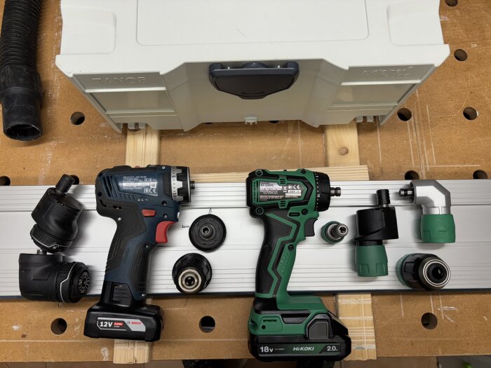 Två borrmaskiner, en Bosch och en Hikoki DS18DDQ, med olika tillbehör, placerade på en arbetsbänk bredvid en förvaringslåda.