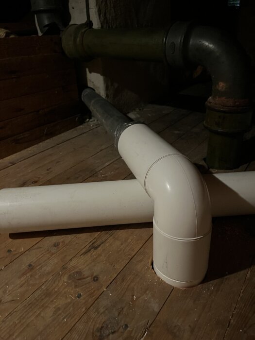 Vita plaströr och äldre plåtrör i ett badrum, kopplade med silvertejp.