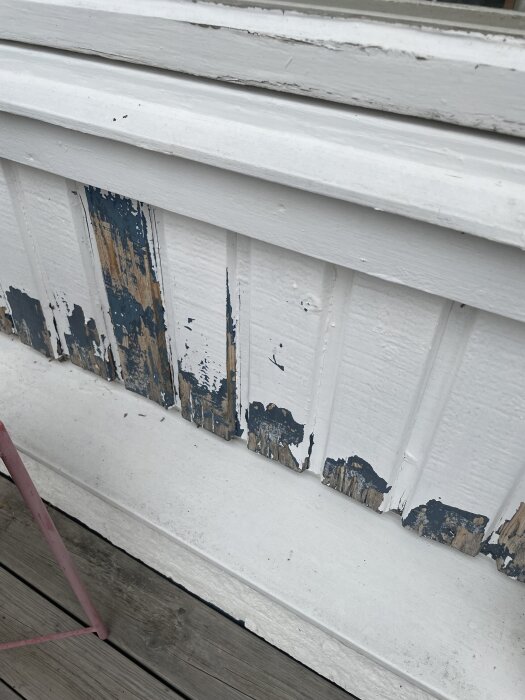 Fasad med avskavd vit färg och synligt trä på en rötskadad panel, del av ett bygge som ska renoveras nästa vår.
