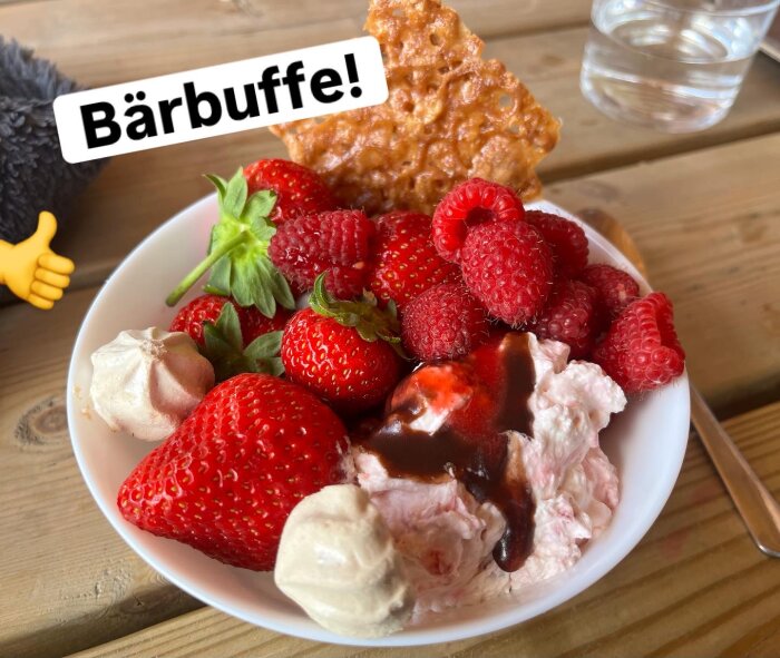 En skål med jordgubbar, hallon, grädde och chokladsås, toppad med maränger och en kaka, märkt "Bärbuffe".