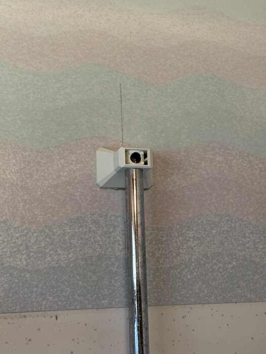 Kromfärgat duschfäste på vägg med vågmönster, visar en skruvhållare för enkel installation av duschset med en skruv.