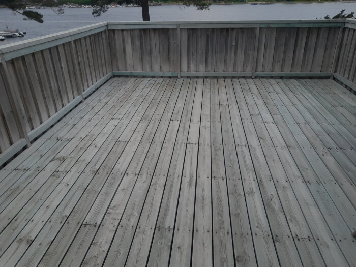 Stor altan i trä med staket, ser nybehandlad ut med bensaltensid enligt Grönfri-metoden. Vatten i bakgrunden, inga synliga skador.