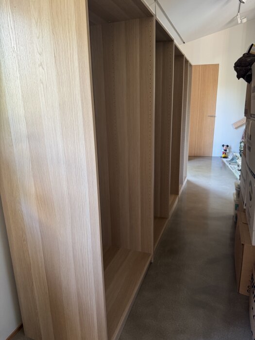 Platsbyggda garderobsstommar i obehandlad träfaner står längs en vit vägg i ett rum under renovering.