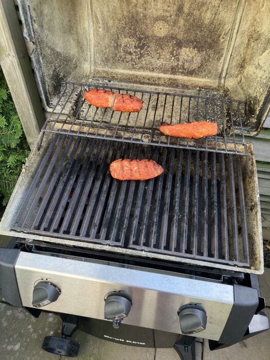 En gasgrill med tre mignoner på gallret, kryddade och klara att grillas, utomhus.