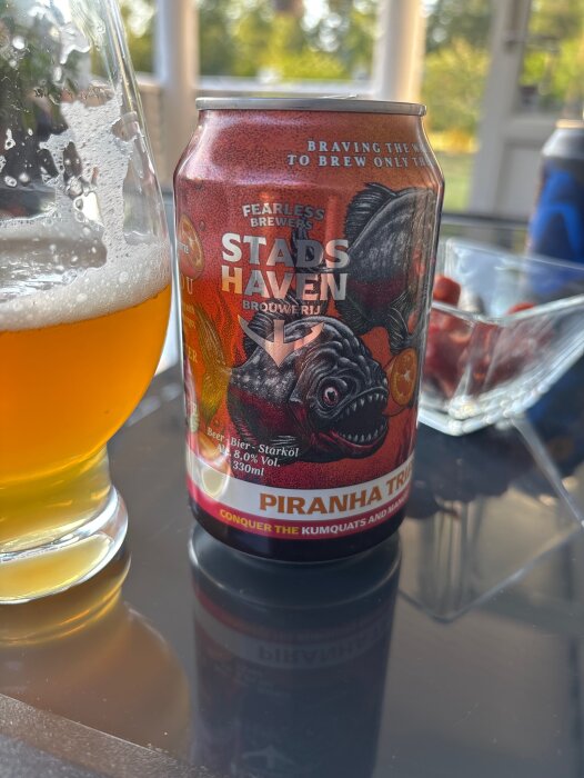 Burk med Piranha Triple öl och ett glas med gyllene öl på ett bord utomhus.