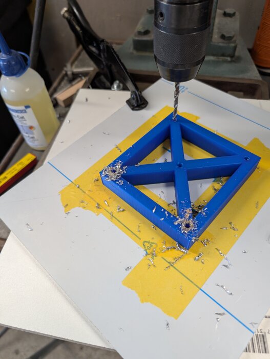 Borrmaskin borrar genom en blå mallfäste på tejpad aluminiumplåt för att montera överhandsfräsen.