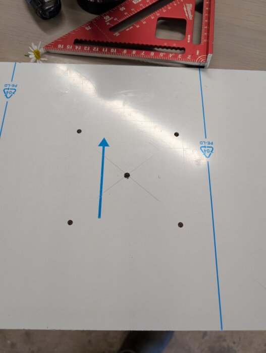 Monteringsmall i aluminium med borrade hål för överhandsfräs, röd vinkelhake synlig.