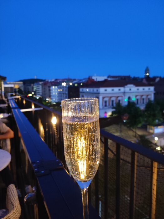 Glas med bubbel på en takbar i Göteborg vid skymningen, staden syns i bakgrunden.