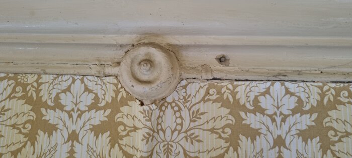 Gammal bakelitdosa och metallrör mot mönstrad tapet i äldre husmiljö.