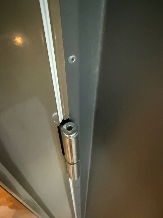 Närbild av ett justerbart dörrgångjärn med insexskruv och en tätningslist intill på en balkong- eller uteplatsdörr.