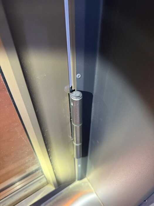 Närbild på ett dörrgångjärn med insexskruv för justering, visar övre delen av gångjärnet på balkong- eller uteplatsdörr.