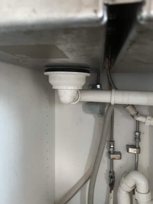 Undersidan av en diskho med avloppsanslutning och rörsystem, där fästet vid utloppet har börjat läcka, i ett köksskåp.