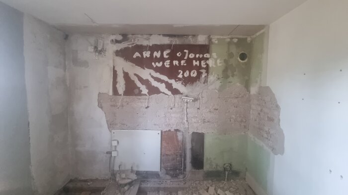 Rivad köksvägg i tegelhus med delar av puts borta, synlig text "Arne o Jonas were here 2007" på brunt underlag.