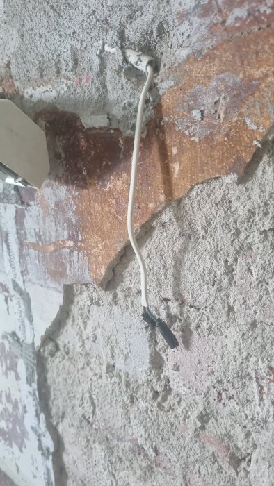 Ojämn tegelvägg med lös puts och synlig vit kabel i gammalt tegelhus från 1926 under köksrenovering.