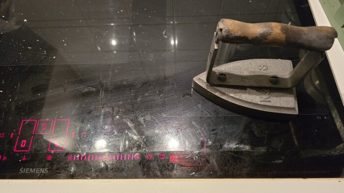 Ett gammalt strykjärn placerat på en induktionshäll med lysande digitala kontroller.