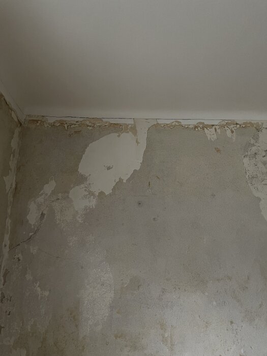 Betongvägg med borttagen tapet och sprickor, delvis skadad yta i behov av renovering.