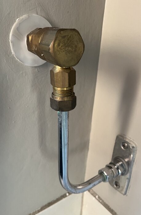 Vinkelkoppling med kromat rör kopplat till väggmonterad anslutning, visar del av vatteninstallation.