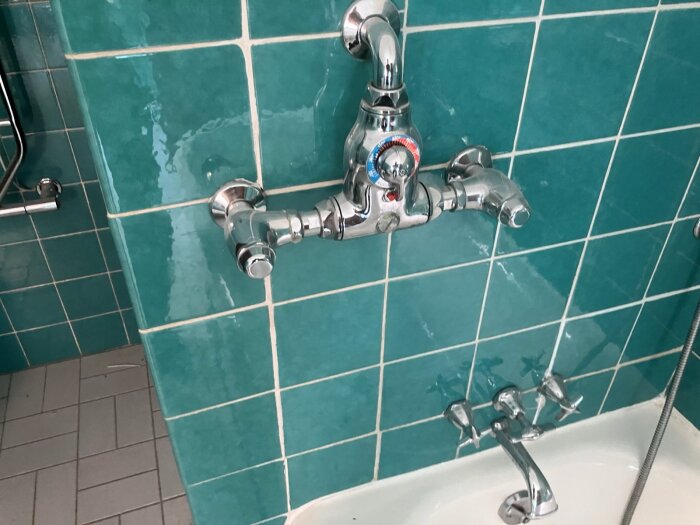 Badrum med turkosa kakelplattor och en kromad duschblandare ovanför ett badkar.