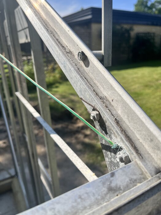 Närbild på metallram del av växthus med skruvar och en grön tråd synlig, förberett för glasmontering.