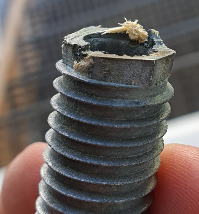 Närbild på en skadad skruv med träflisor fast i toppen. Skruven verkar ha använts i karmfixering av en altandörr.