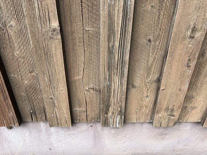 Vertikala träpaneler på en yttervägg som visar slitage och behov av byten.