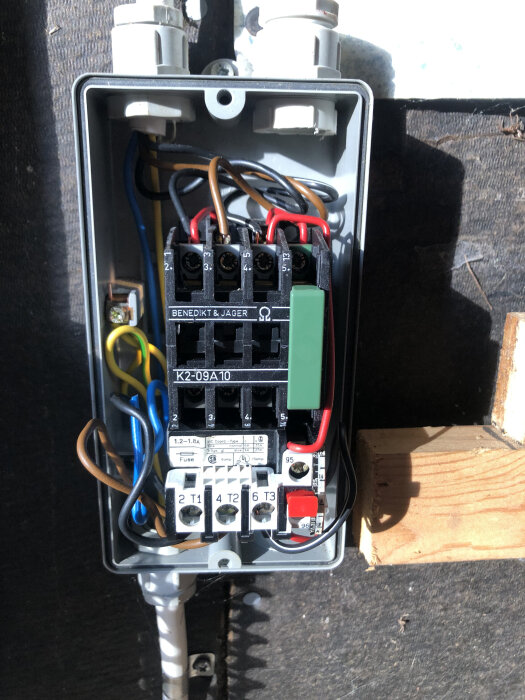 Elektrisk kopplingsbox med Benedikt & Jäger motorrelä, synliga kablar och färgkodade knappar i en brunnen installation.