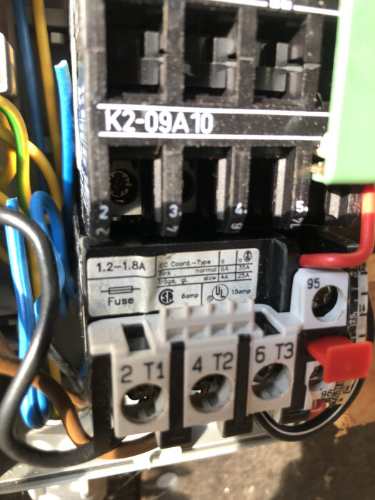 Närbild av elektrisk kontaktor märkt K2-09A10 med flera anslutningar och märkskylt, visas även säkringar och kabeluppkopplingar.