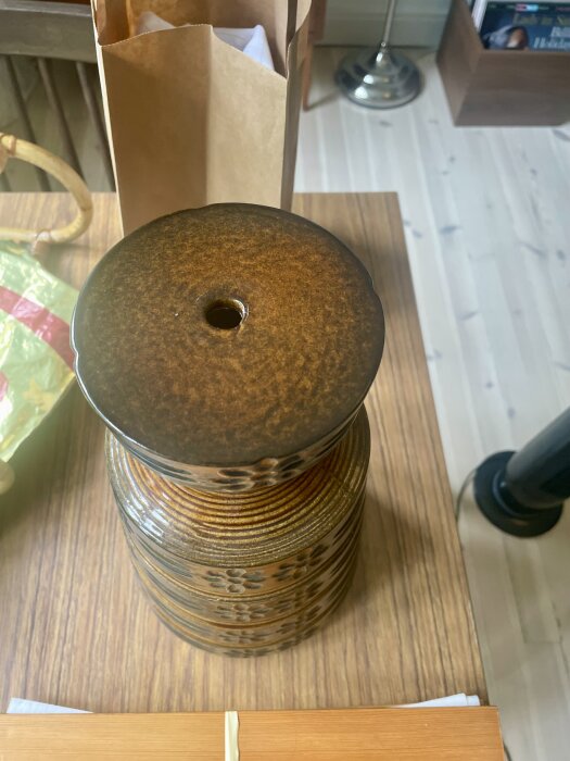 Keramisk lampfot i brunt med ett hål upptill för montering av lamphållare, stående på ett träbord.