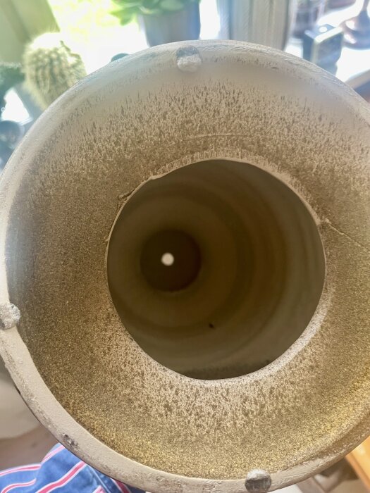 Närbild av undersidan av en lampfot med hål för montering av el. Lampfoten har ojämn yta med smuts eller slitage runt kanten.