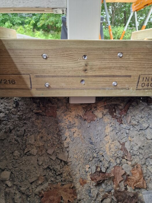 Träreglar i en konstruktion, fästa ihop med metallskruv, ovanpå krossad sten och jord.