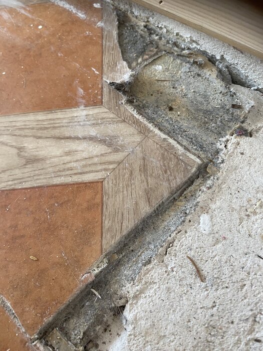 Närbild på linoleumgolv med väv, svart underlag och ett hörn där mattan delvis saknas, avslöjande en betongyta under.