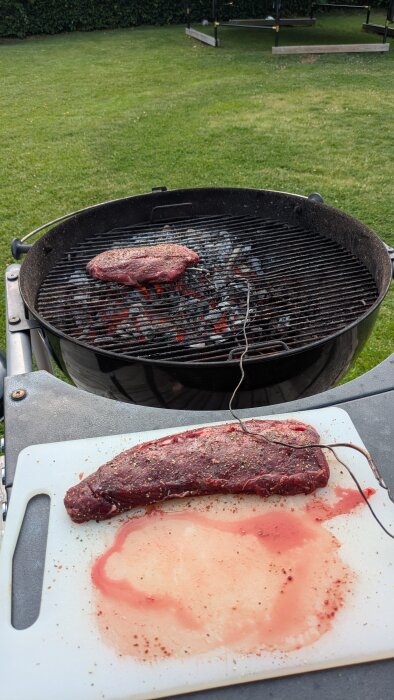 Grillad mufflonköttbit på utegrill och en annan köttbit på skärbräda, redo för tillagning.