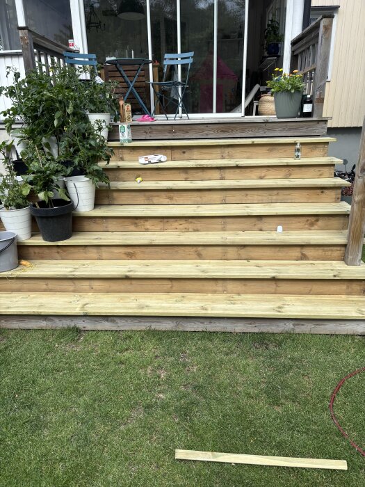 Ny trapptrall med ljusa träplankor, omgivna av krukväxter och en sittgrupp vid entrén till uteplatsen.