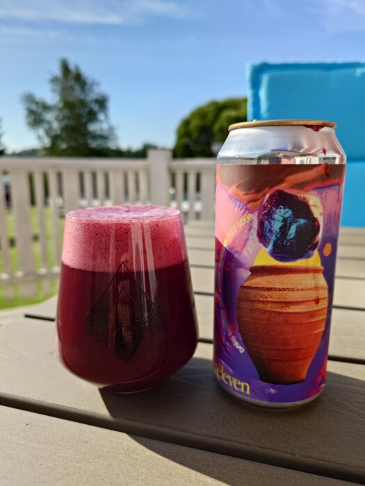 En burk Elmeleven - Spase öl och ett glas med syrlig röd öl på ett bord utomhus.