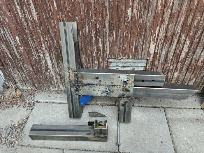 Svetsade metallbitar på cementplattor framför en gammal trävägg, visar kreativ användning av svetsverktyg.