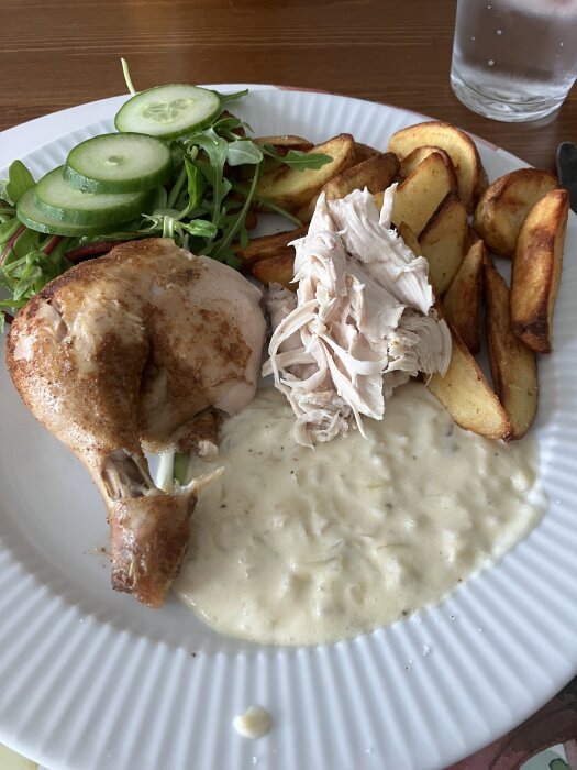 Tallrik med kyckling, klyftpotatis och gorgonzolasås, serverad med sallad och gurkskivor.