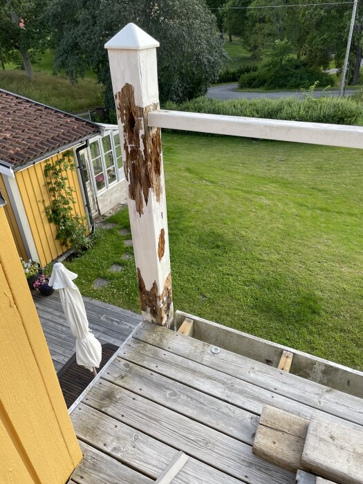 Ruttna delen på en vit balkongstolpe, sett från ovan, med trädgård och hus i bakgrunden.