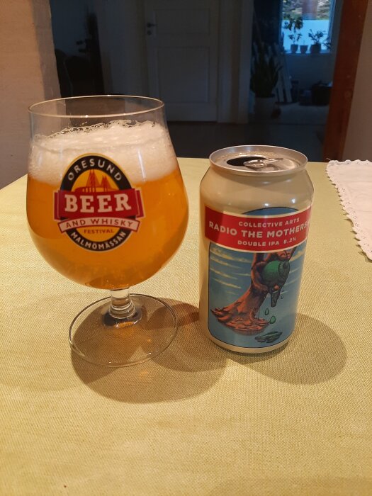 Ett glas och en burk med kanadensisk dubbel IPA-öl, märkt "Radio the Mothership" från Collective Arts, på ett bord.