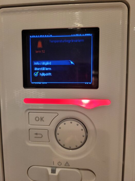 Närbild på en värmepumpsdisplay som visar "Temperaturbegränsarlarm larm 52" med alternativ för återställning och hjälpdritt.