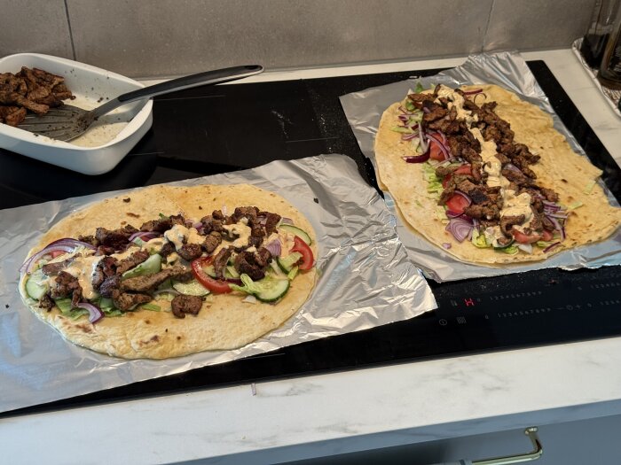 Hemgjorda kebabrullar med kött, grönsaker och sås på hembakat bröd, serverade på aluminiumfolie i köket.